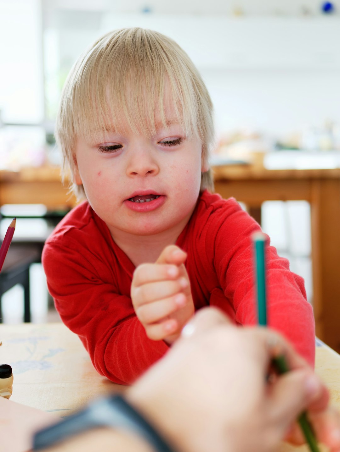 A young boy with Down syndrome draws with his parent.